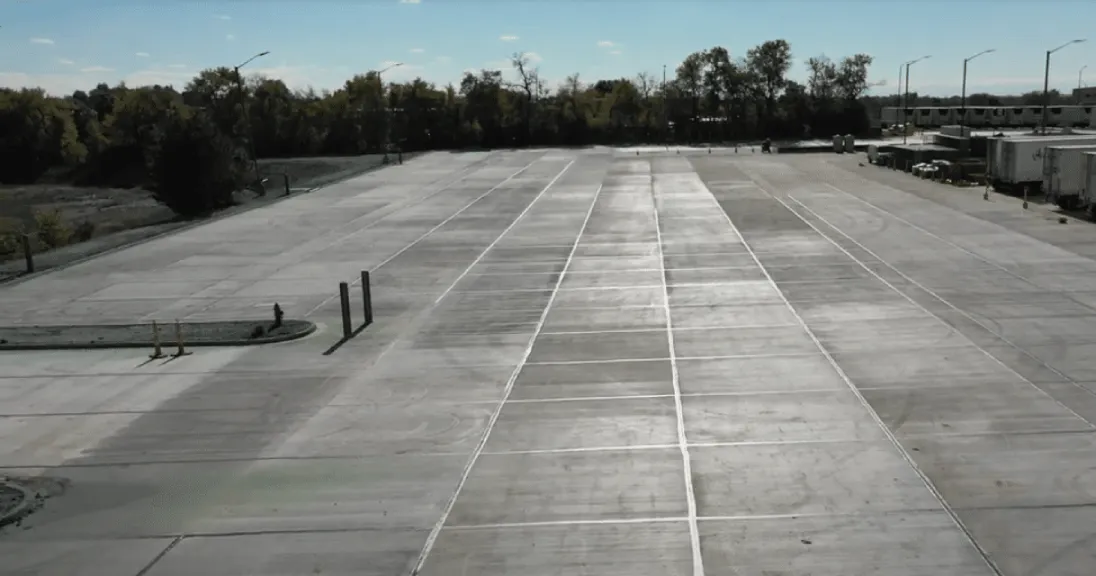A truck driving on a large concrete parking lot.